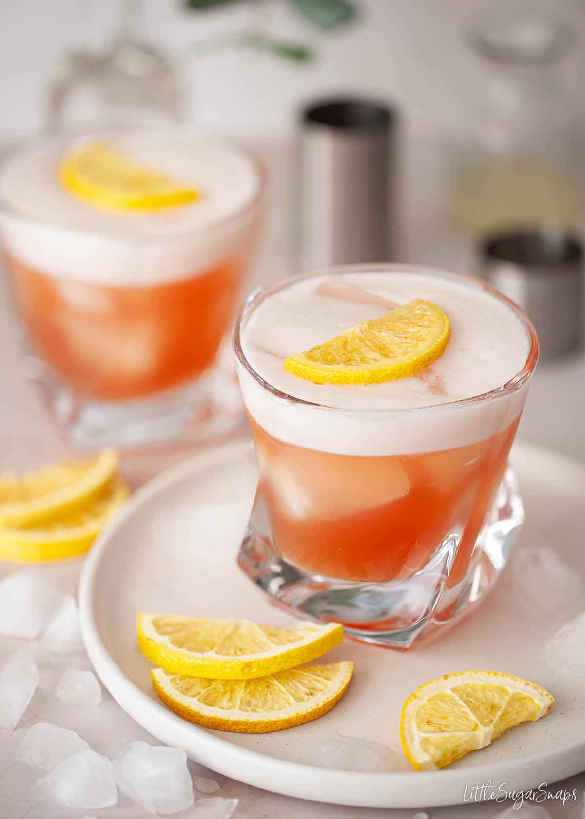 Two glasses of Negroni sour with egg white foam and lemon slice garnish on the top.