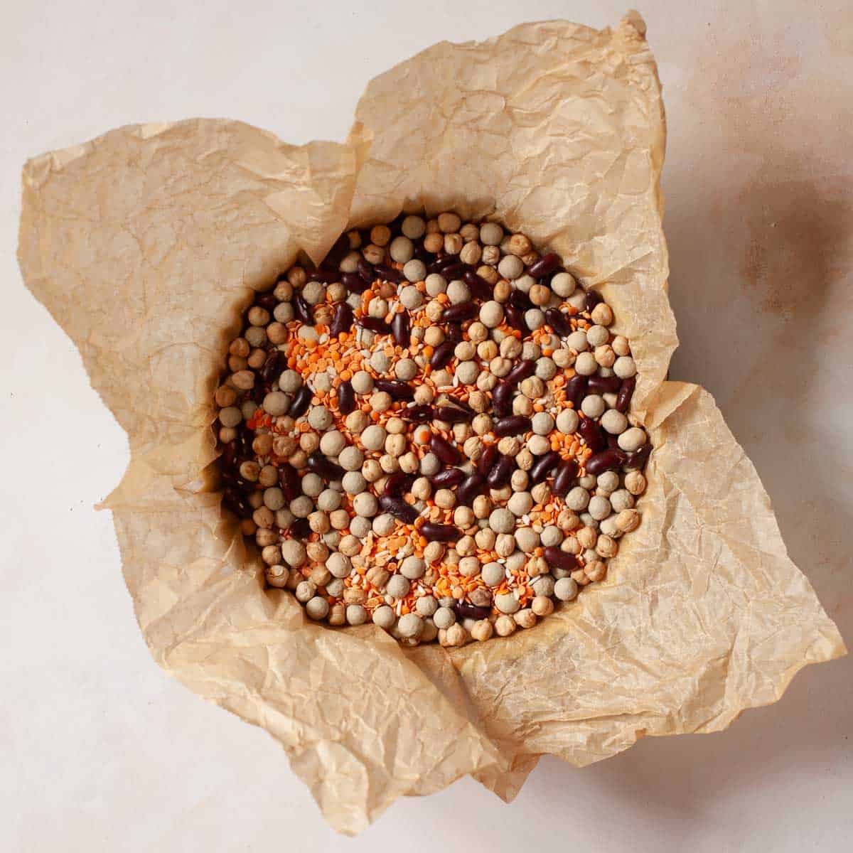 A tart tin lined with parchment and mixed pulses ready for blind baking.