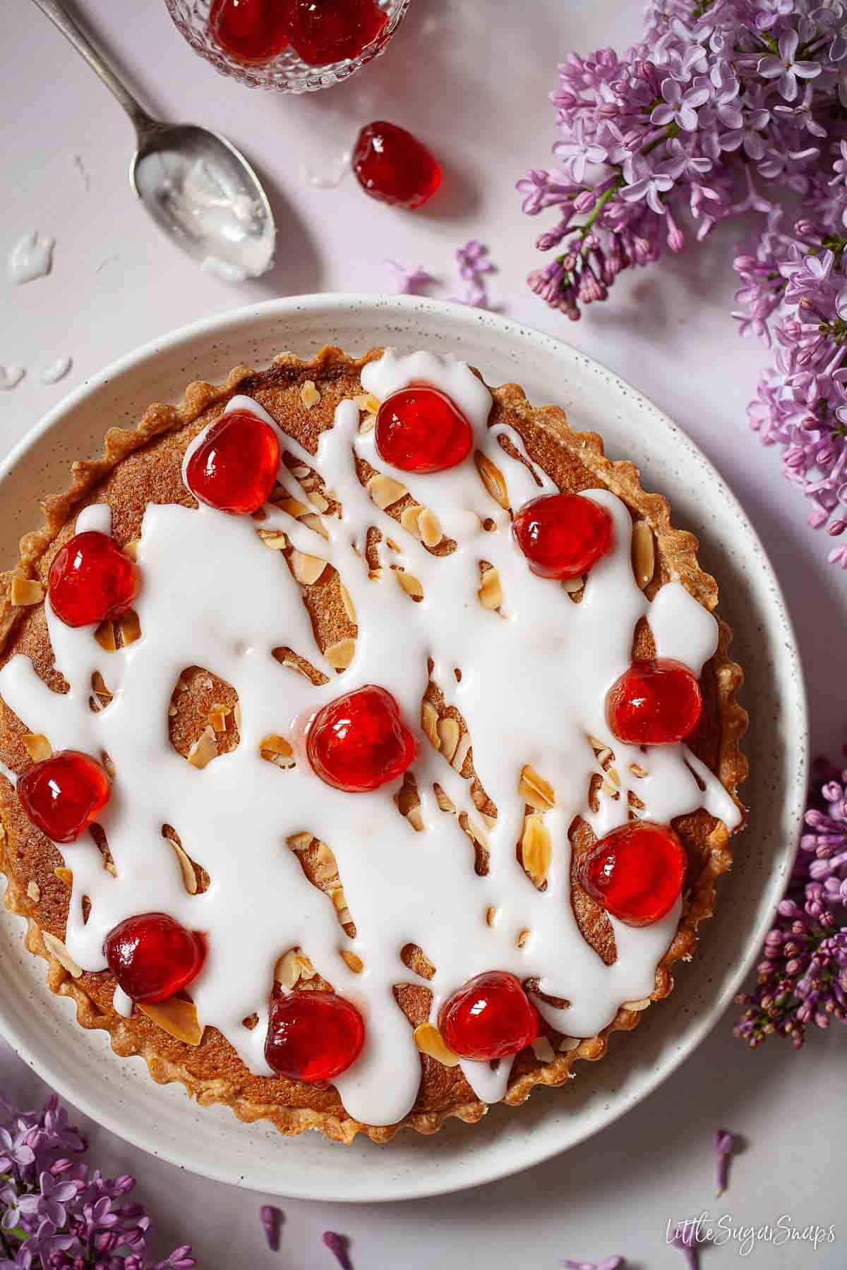 Cherry Bakewell tart topped with glacé icing and candied cherries with a bowl of cherries.