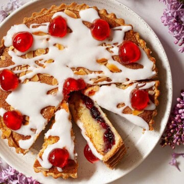 Close up image of cherry Bakewell tart topped with glacé icing and red glacé cherries.