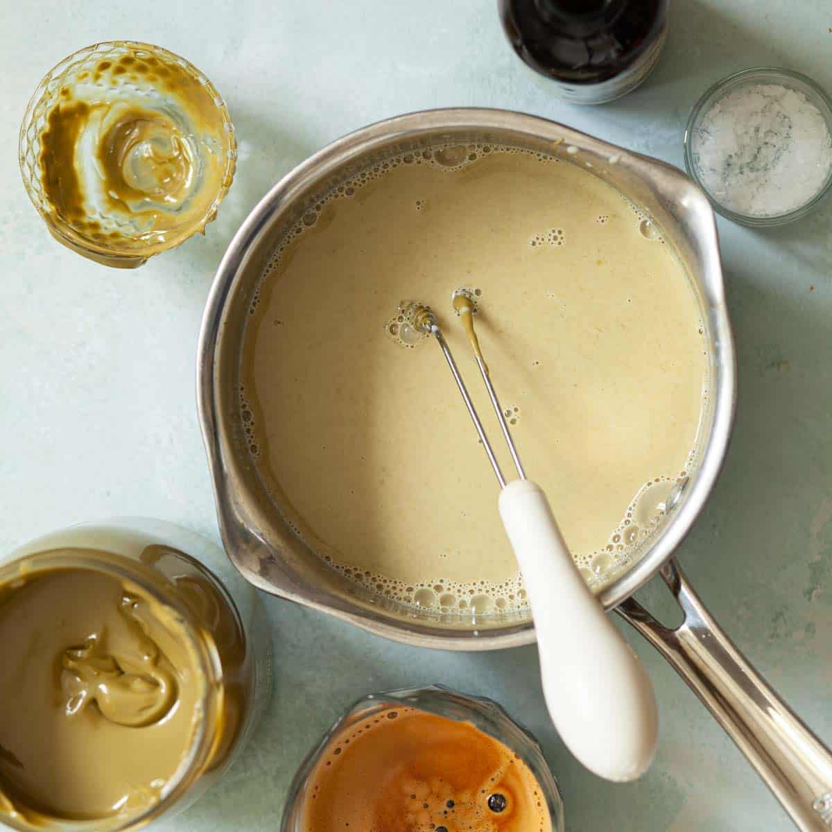 Pistachio flavoured milk in a saucepan with a small handheld whisk in the pan too.