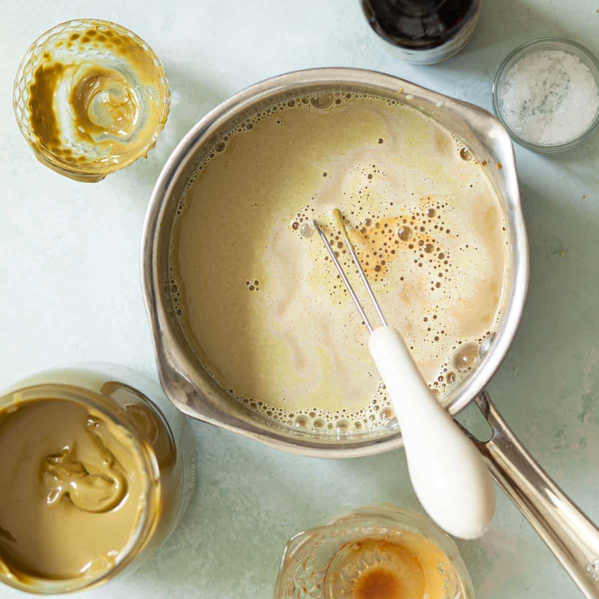 A handheld ballon whisk in a pan with pistachio coffee.