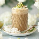 Close up of a pistachio latte with whipped cream, pistachio sauce and chopped pistachio nuts.