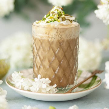 Close up of a pistachio latte with whipped cream, pistachio sauce and chopped pistachio nuts.