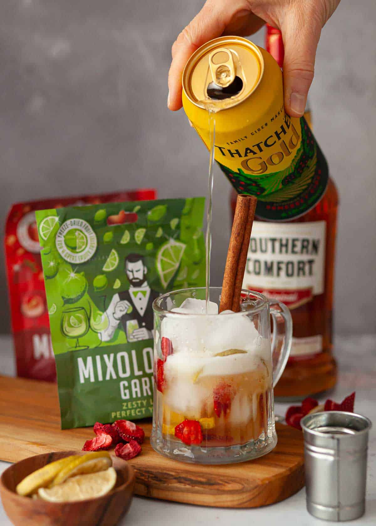 Cider being poured into a tankard with ice, fruit pieces and Southern Comfort.
