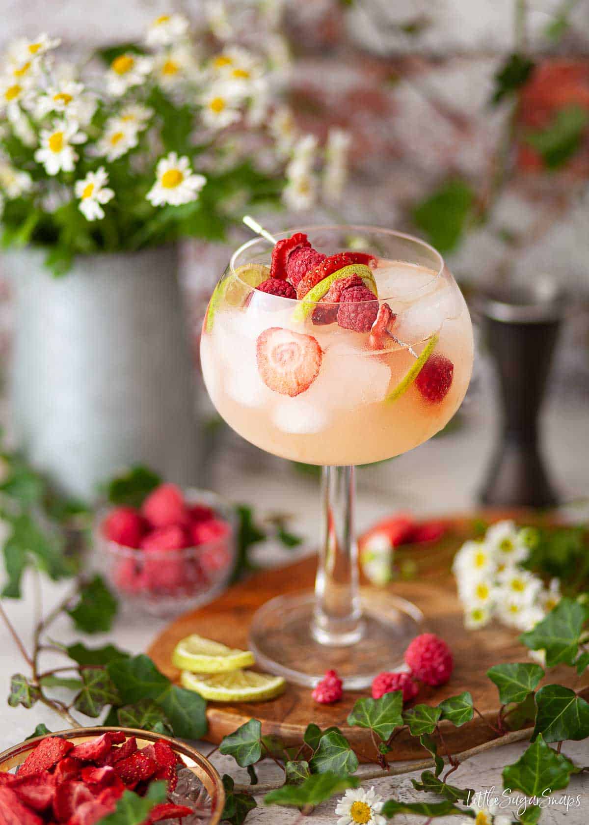 An English garden gin and apple juice cocktail with freeze-dried fruit on a cocktail pick as garnish.