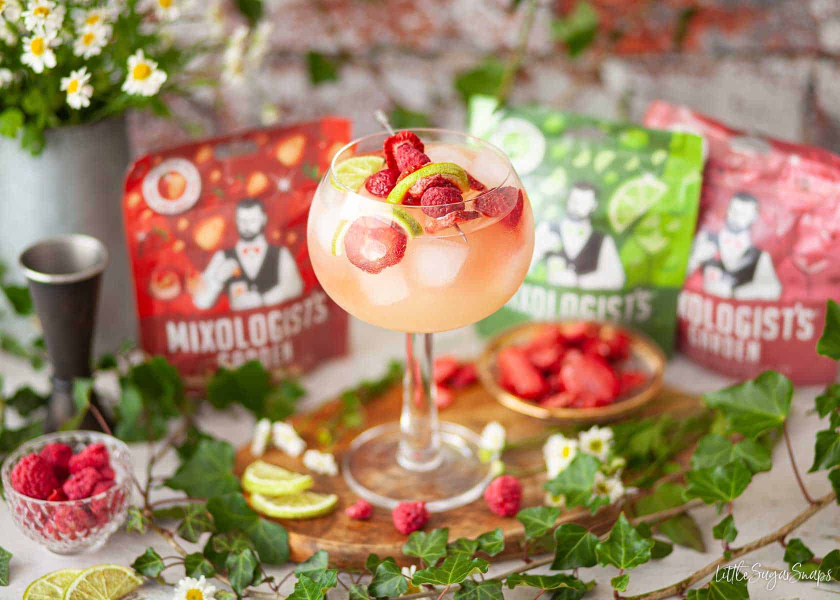 A gin, elderflower and apple juice drink with foliage and packaging surrounding it.