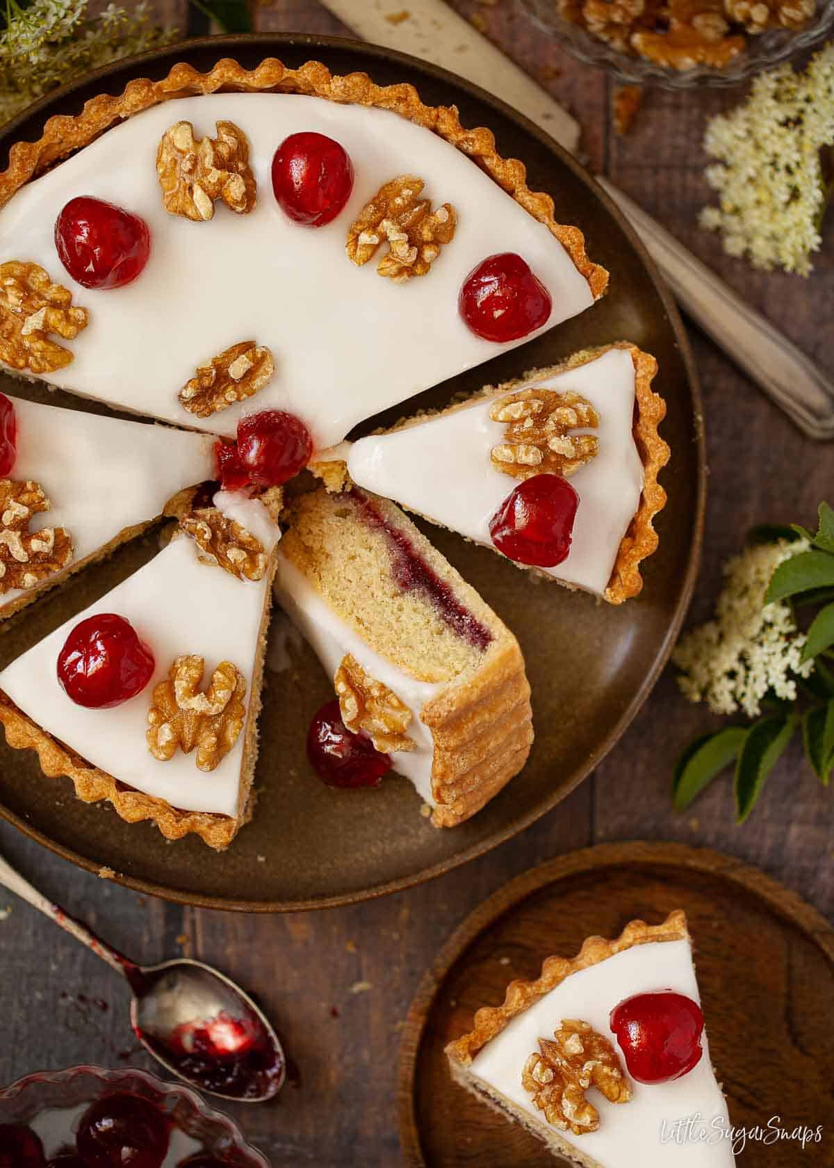 Partially sliced Trentham tart topped with glacé icing, glacé cherries and walnuts.