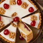 Partially sliced Trentham tart topped with glacé icing, glacé cherries and walnuts.