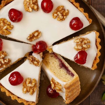 Partially sliced Trentham tart topped with glacé icing, glacé cherries and walnuts.