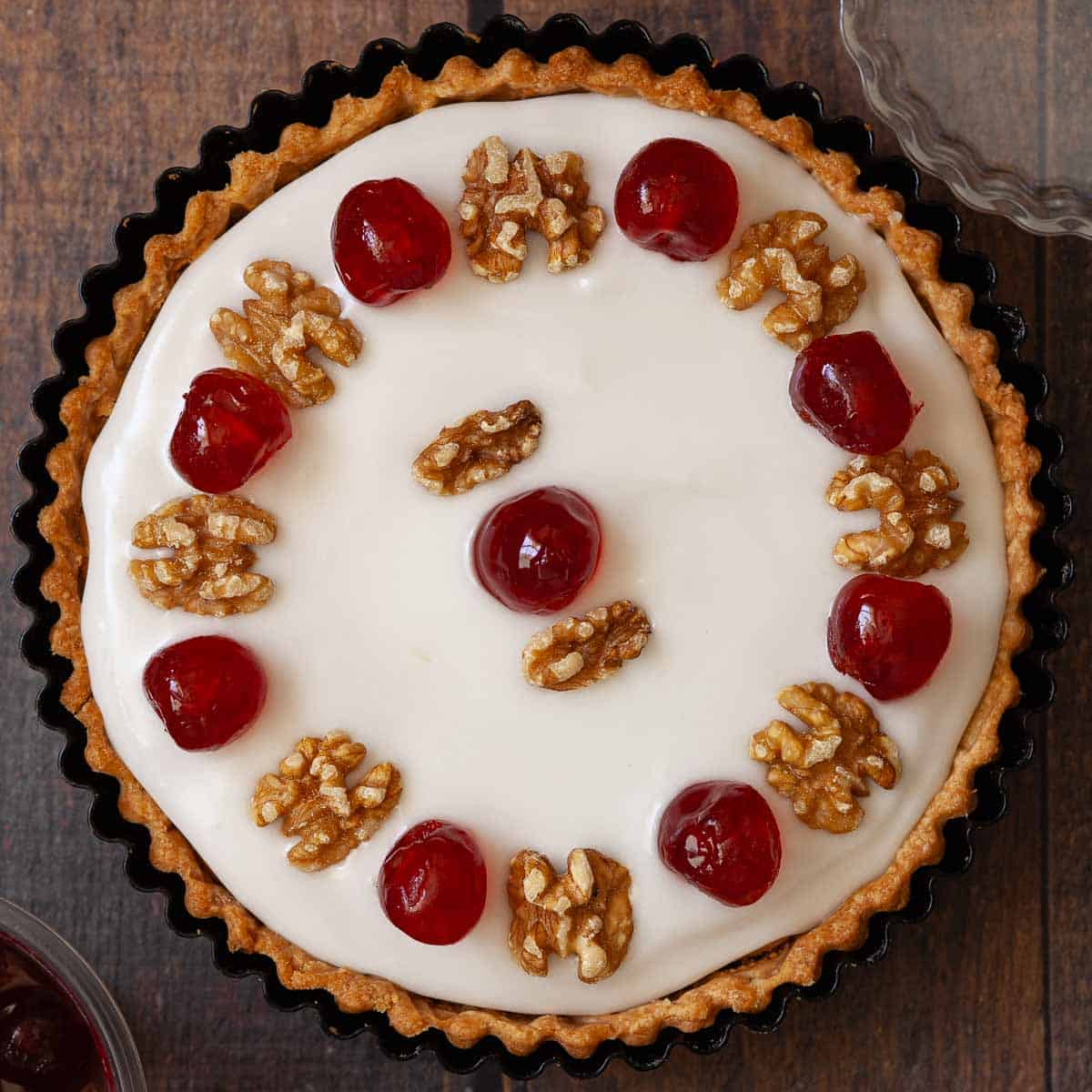 A jam sponge tart topped with glacé icing, candied cherries and walnuts.