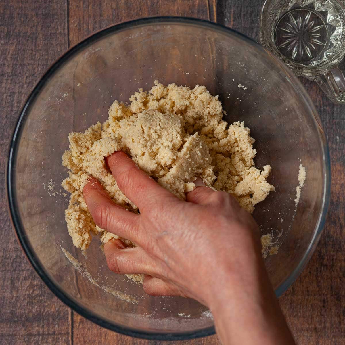 A hand in a bowl forming shortcrust pastry dough.