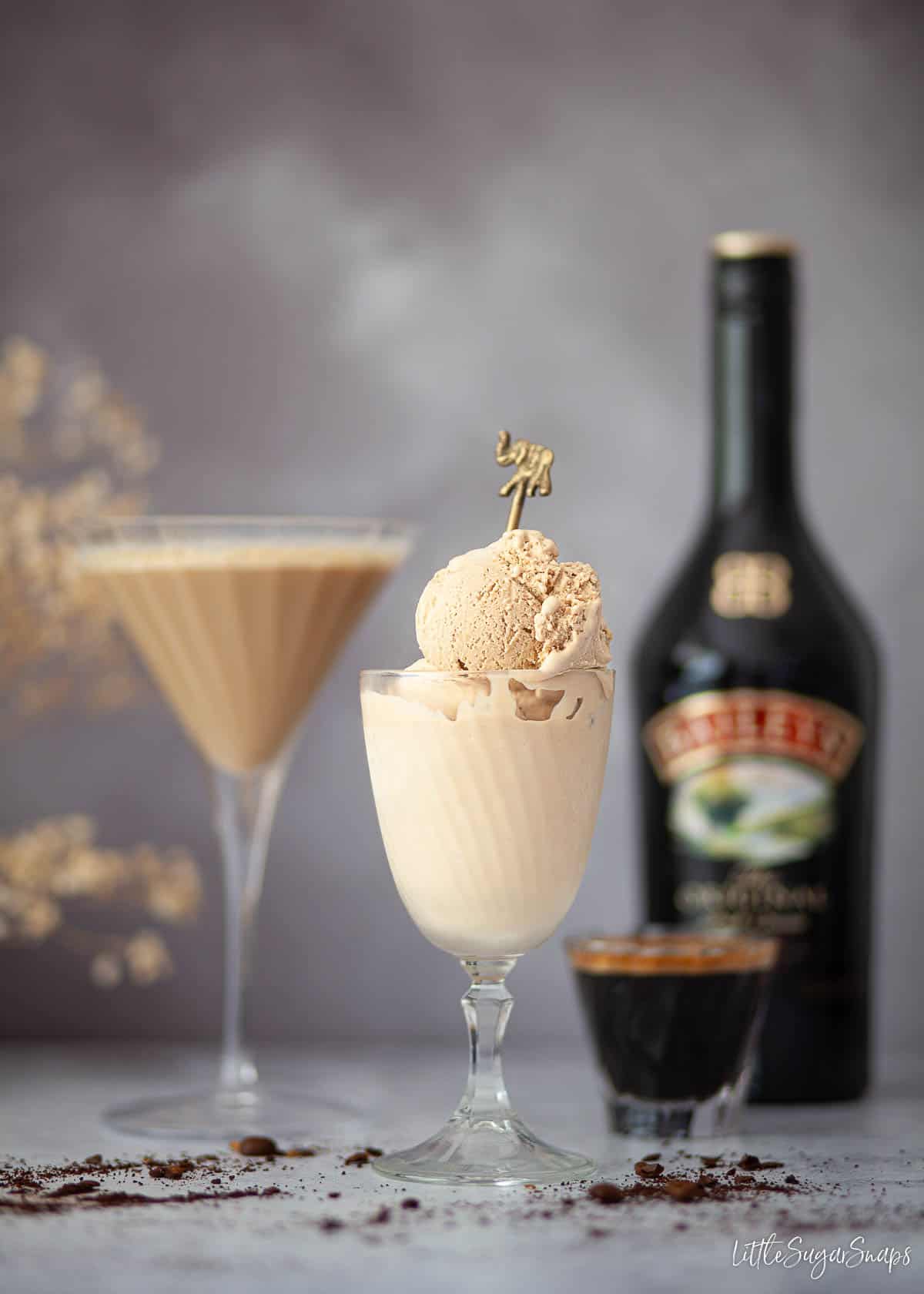 Baileys espresso martini ice cream in a glass with a cocktail and botte of Irish Cream in the background.