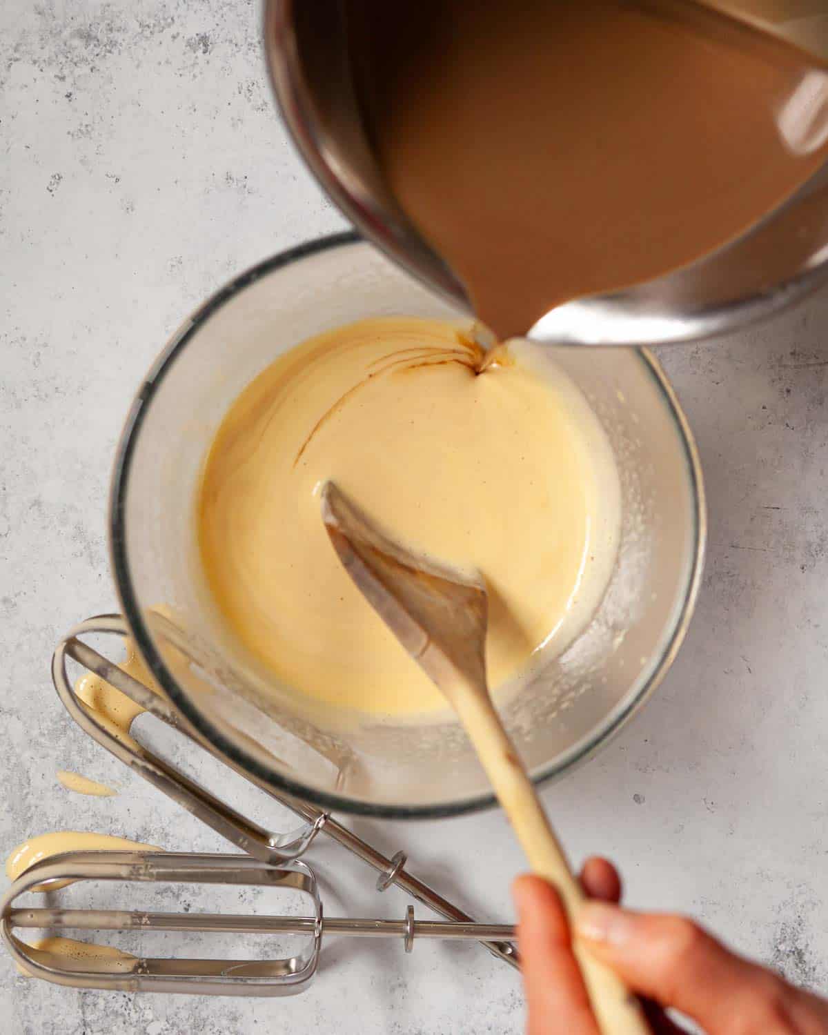 Coffee infused milk being poured into whisked egg yolk.