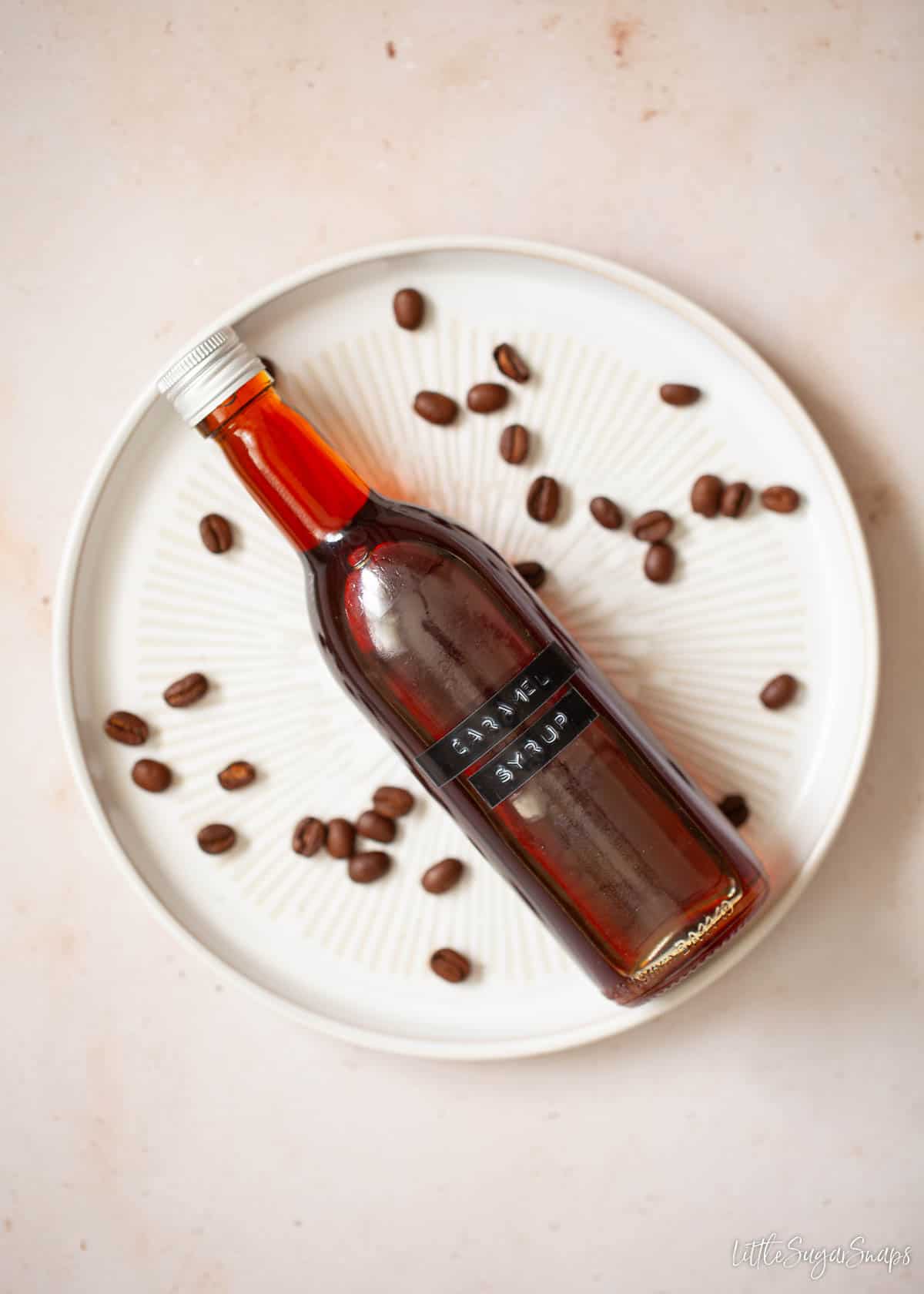 A bottle of caramel simple syrup on a plate with coffee beans scattered around.