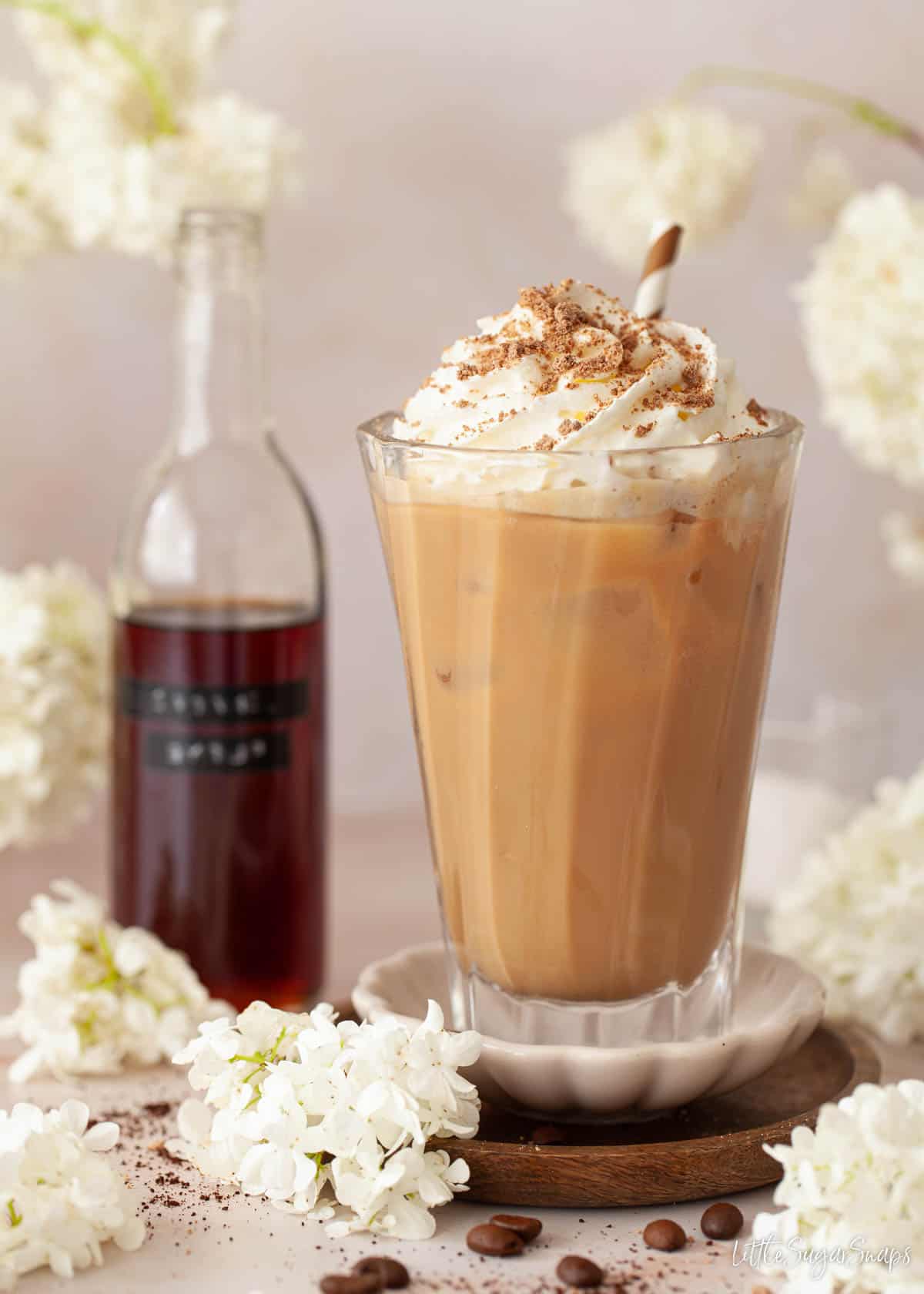 An iced caramel coffee drink with a bottle of caramel syrup in the background.