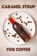 Labelled image of a bottle of caramel simple syrup on a plate woth coffee beans.