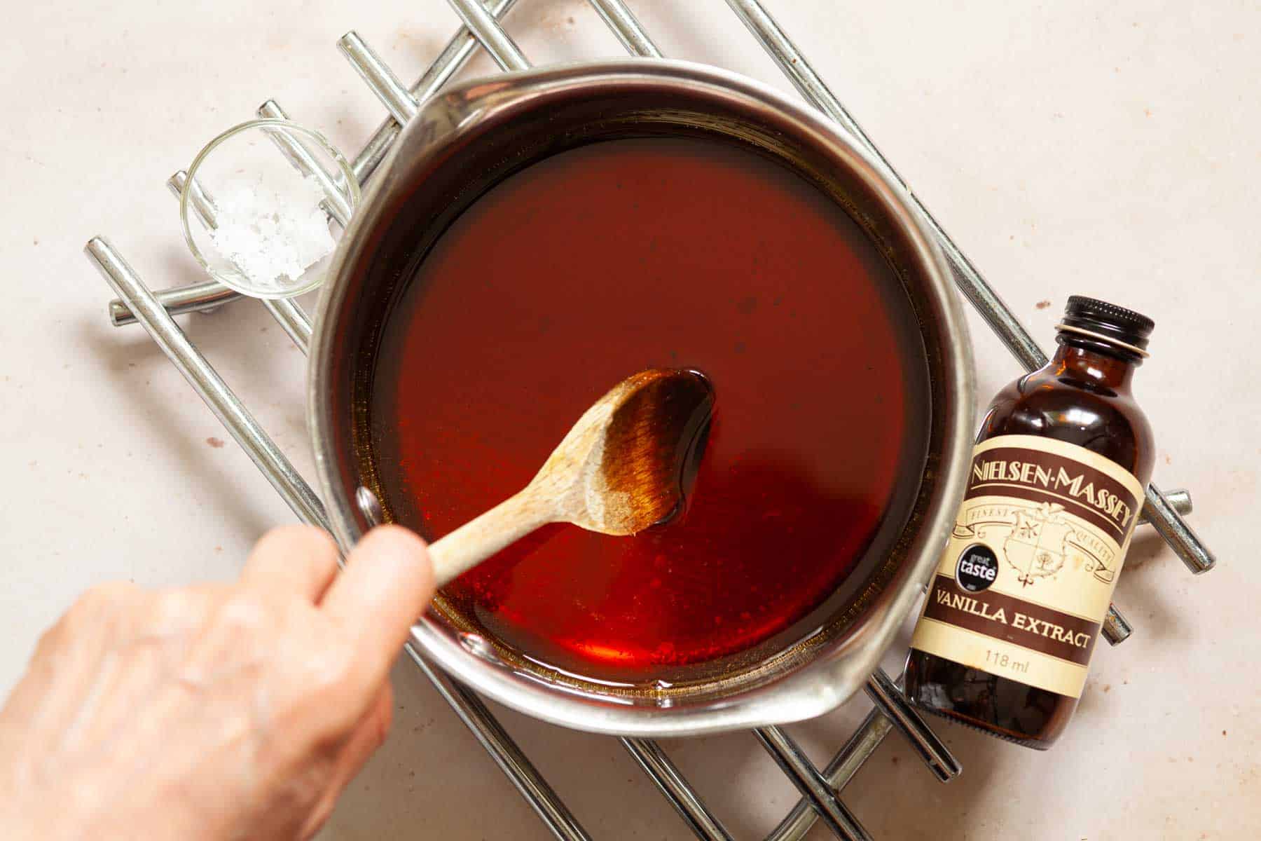 Vanilla extract being stirred into caramel syrup in a saucepan.