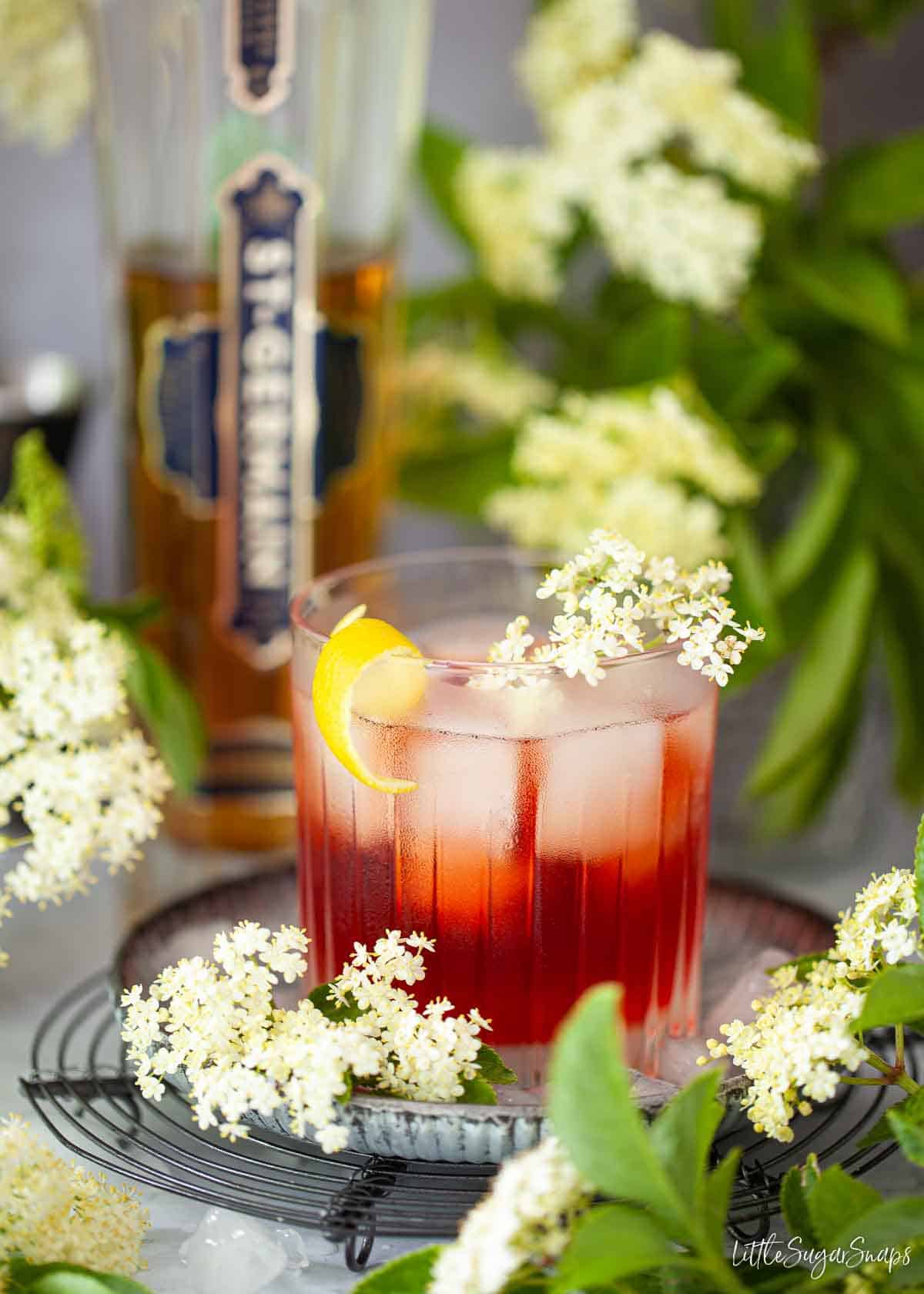 A gin and elderflower cocktail with a bottle of St Germain in the background.