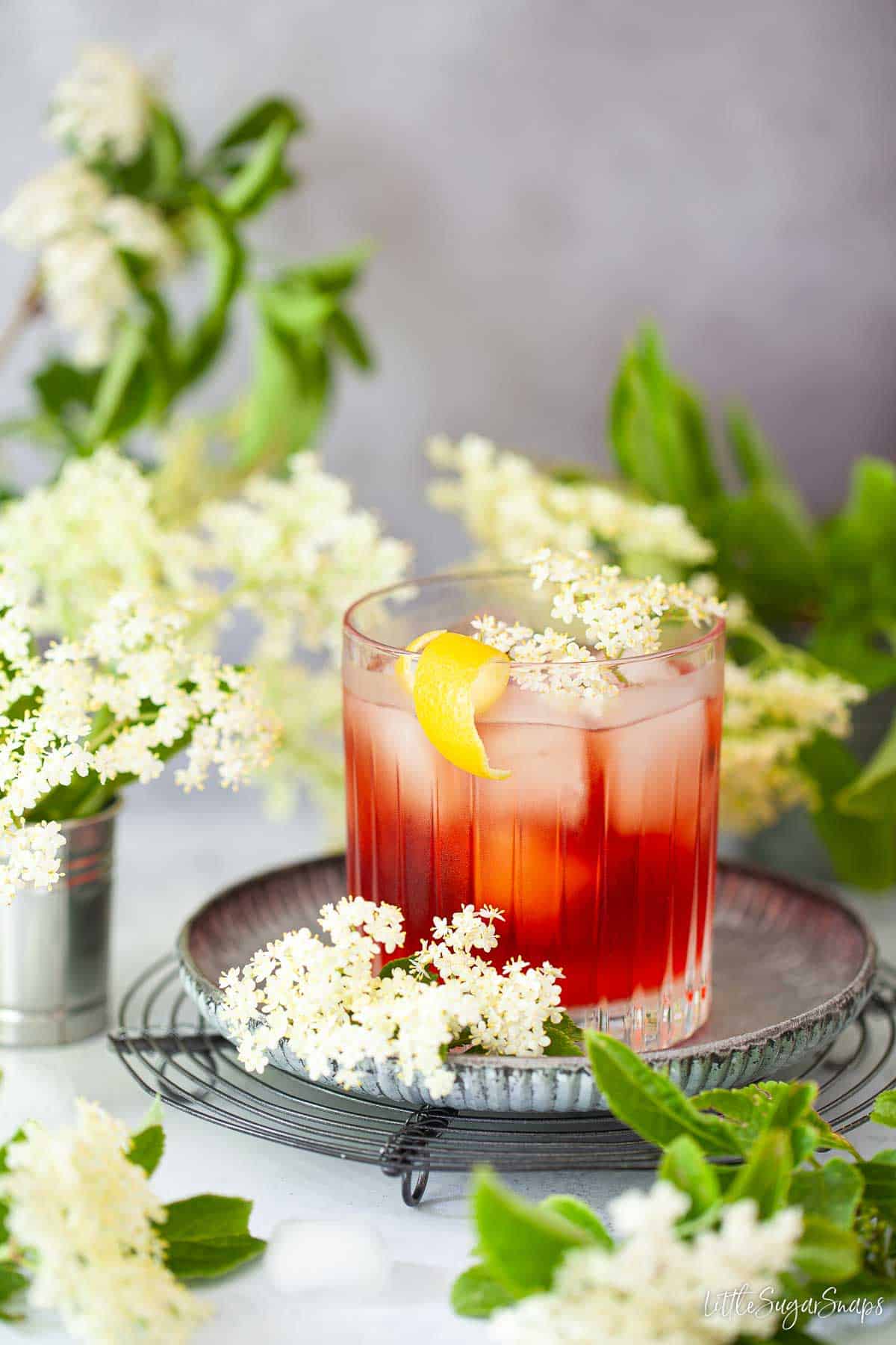 A gin and elderflower cocktail garnished with lemon zest and fresh elderflowers.