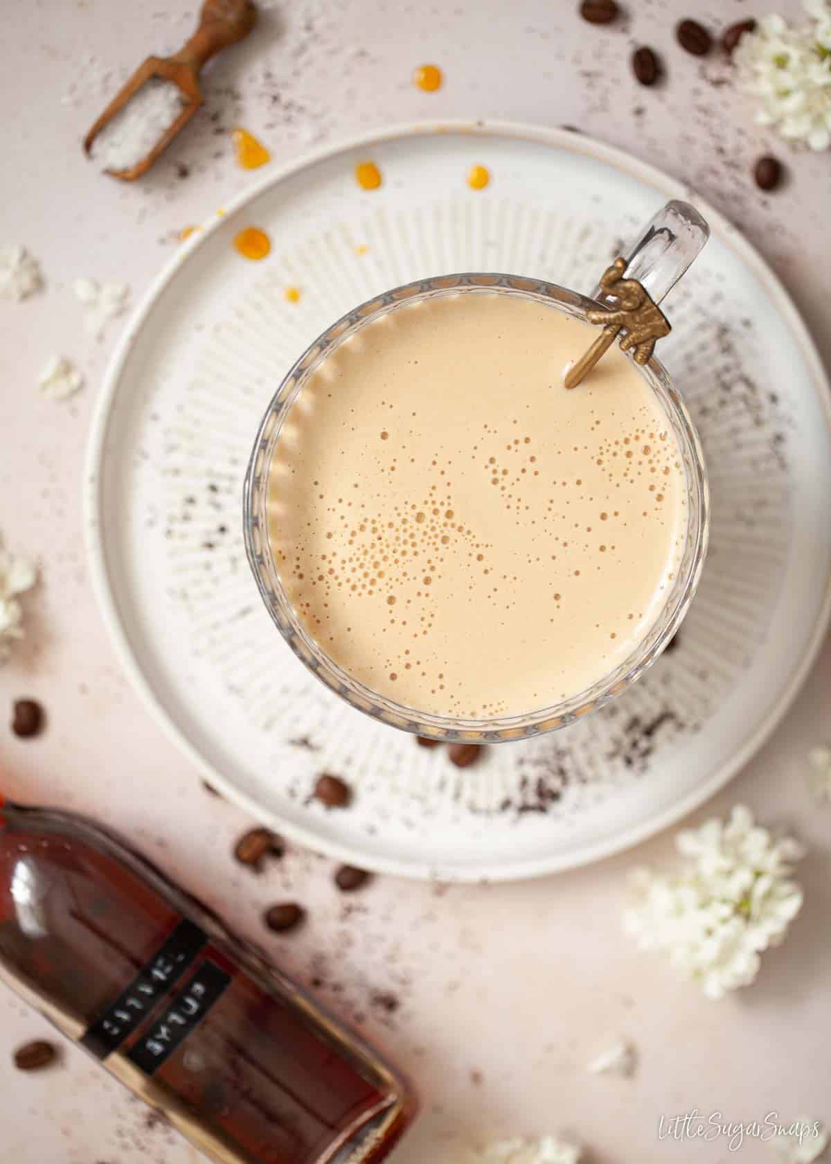 A frothy caramel coffee drink in a glass mug with ingredients around it.