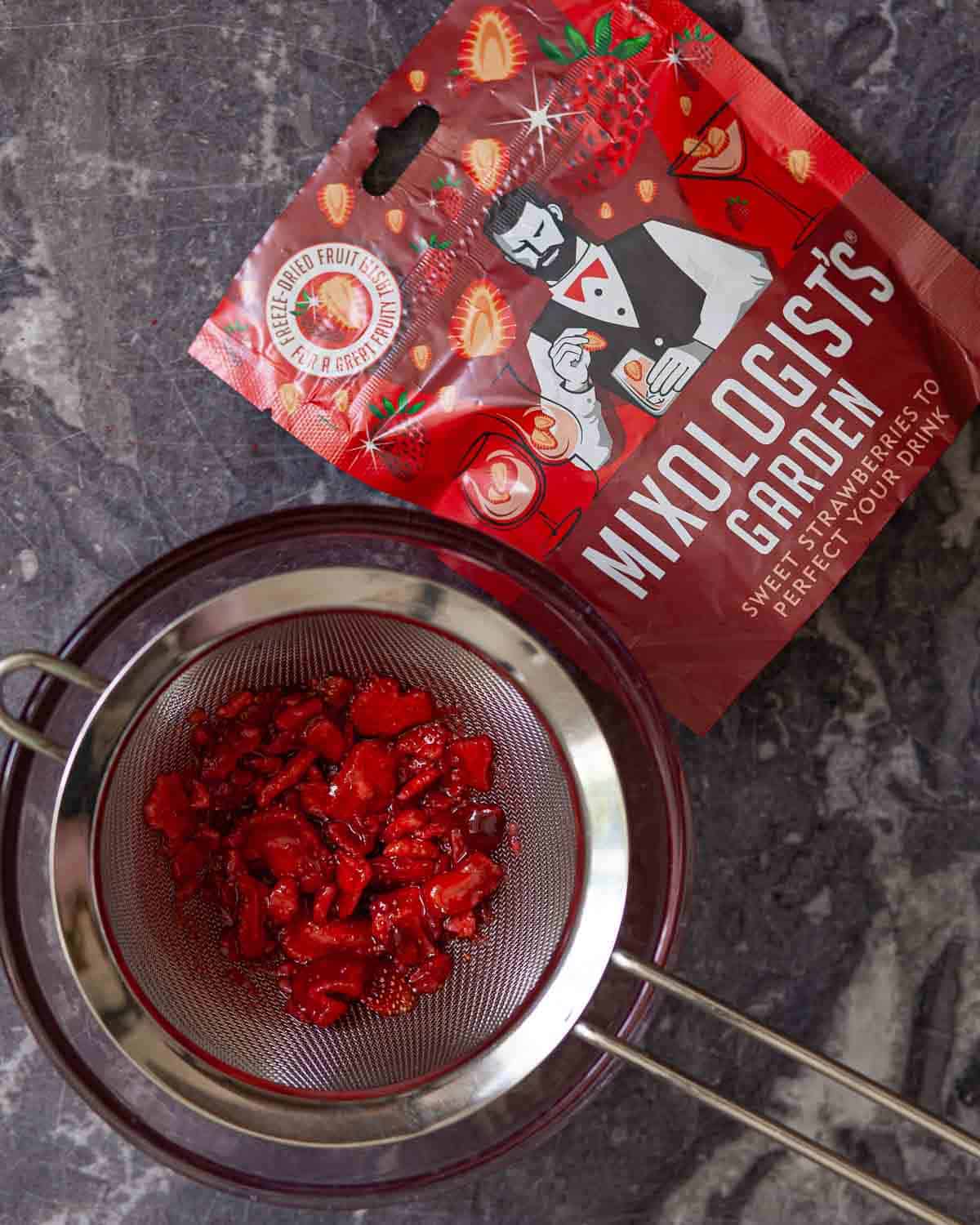 Strawberry cocktail syrup being strained through a sieve to remove the fruit.