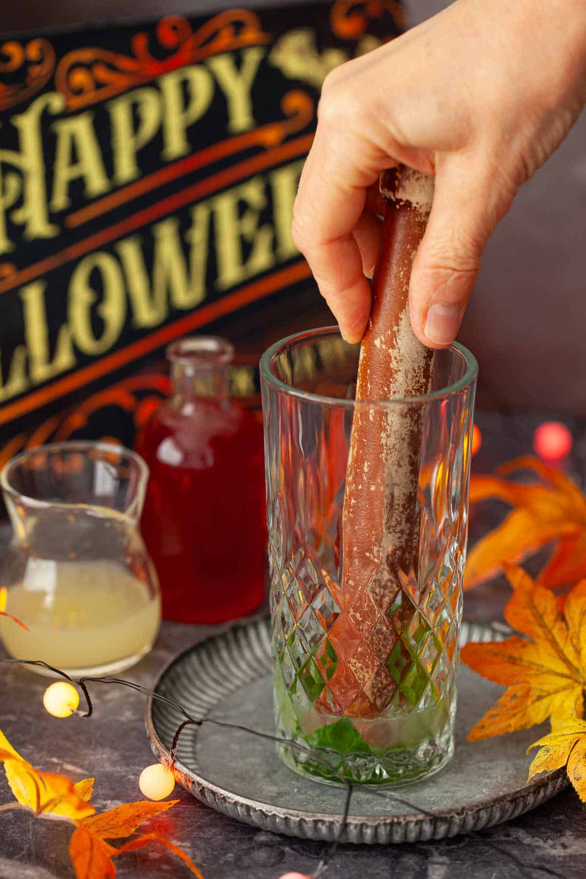 A person bruising mint leaves in a glass with a muddling stick.