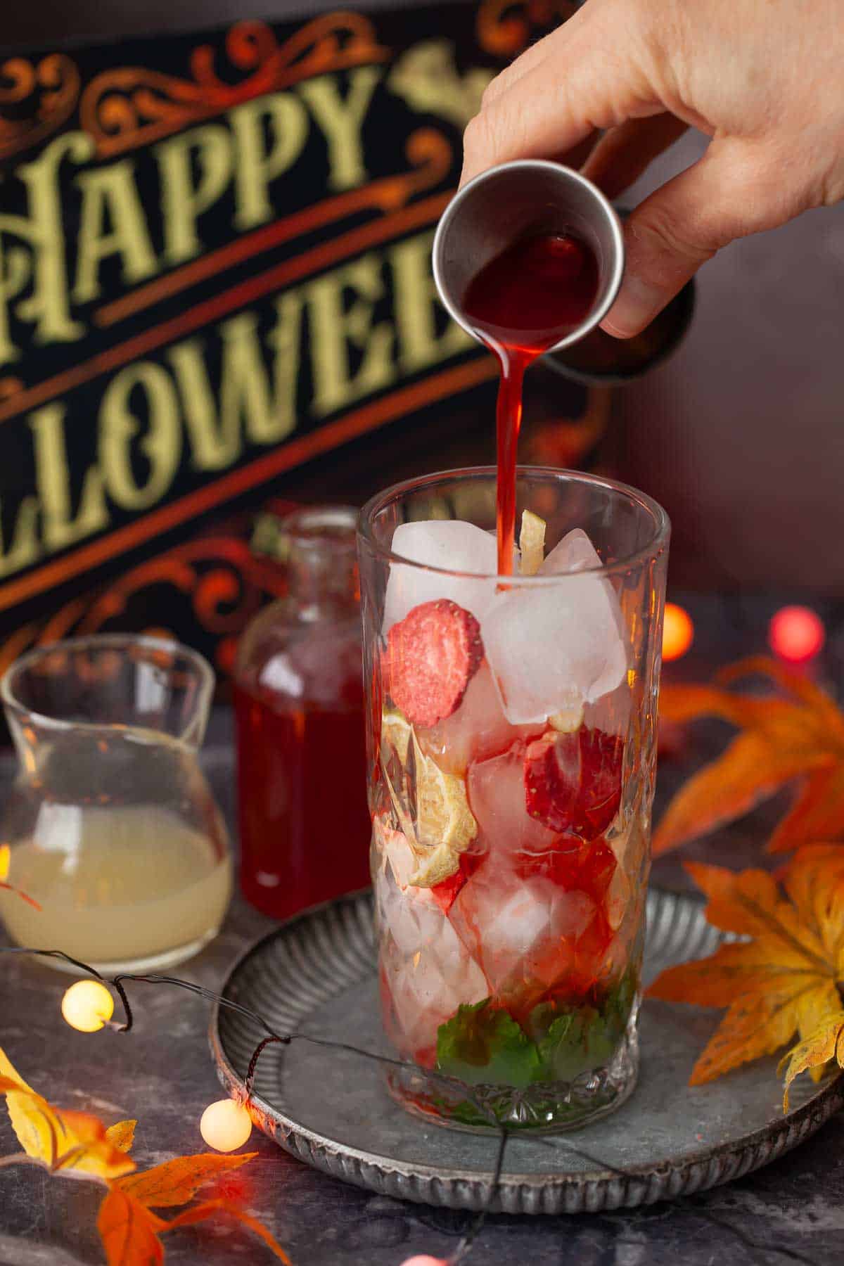 A person pouring strawberry cocktail syrup into a glass filled with ice.