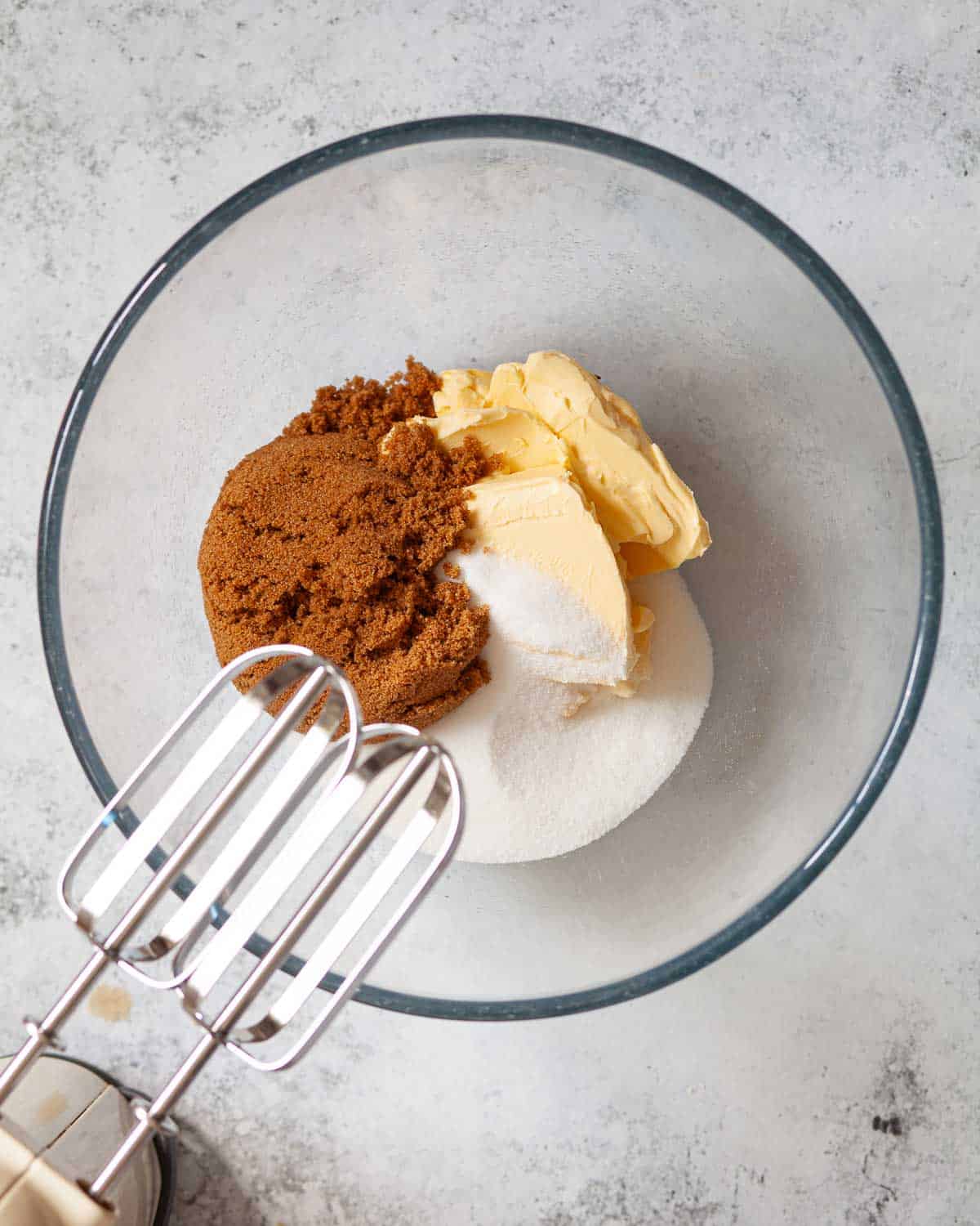 Butter, white sugar and brown butter in a mixing bowl with electric beaters overhead.