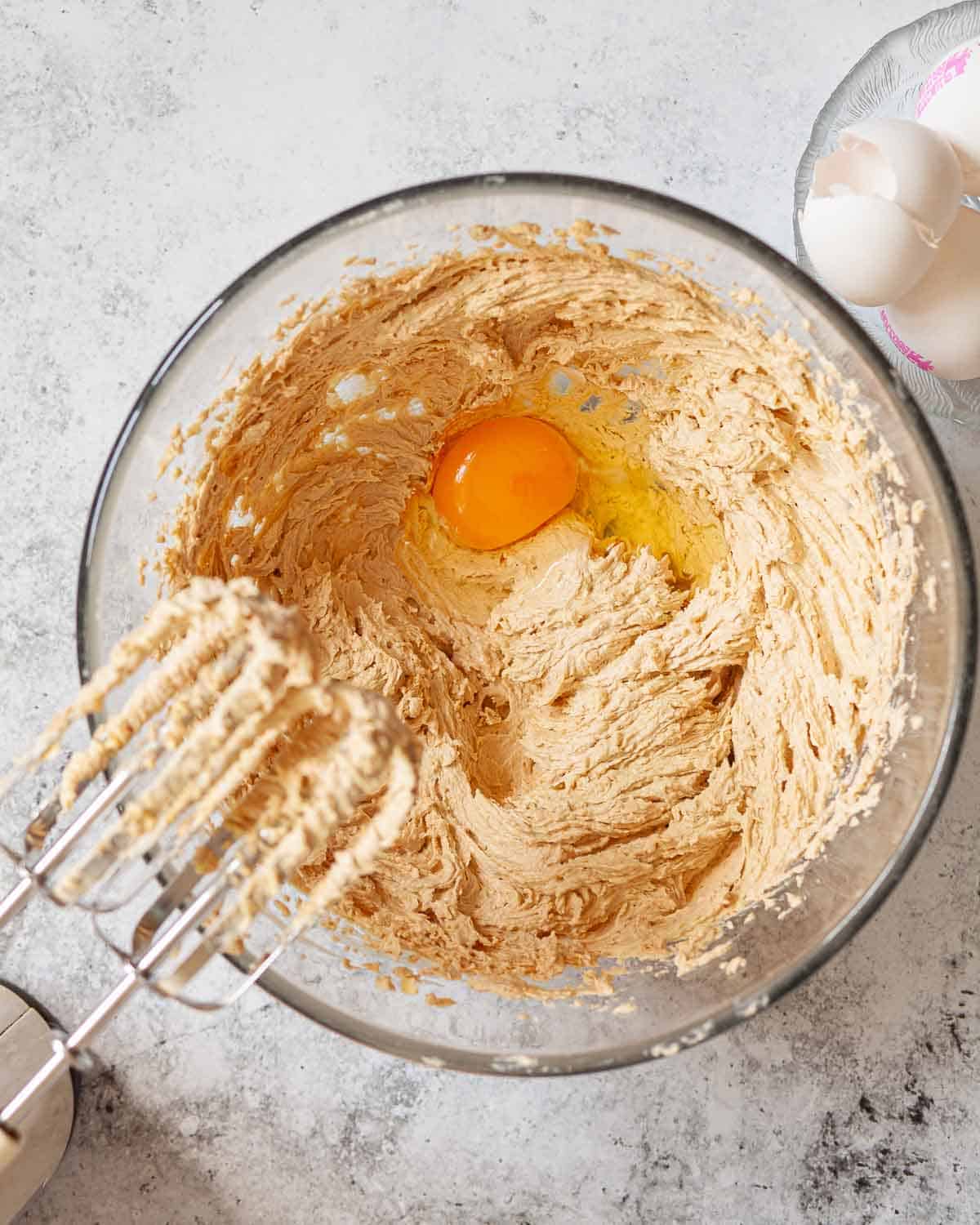 An egg about to be beaten into creamed butter and sugar.