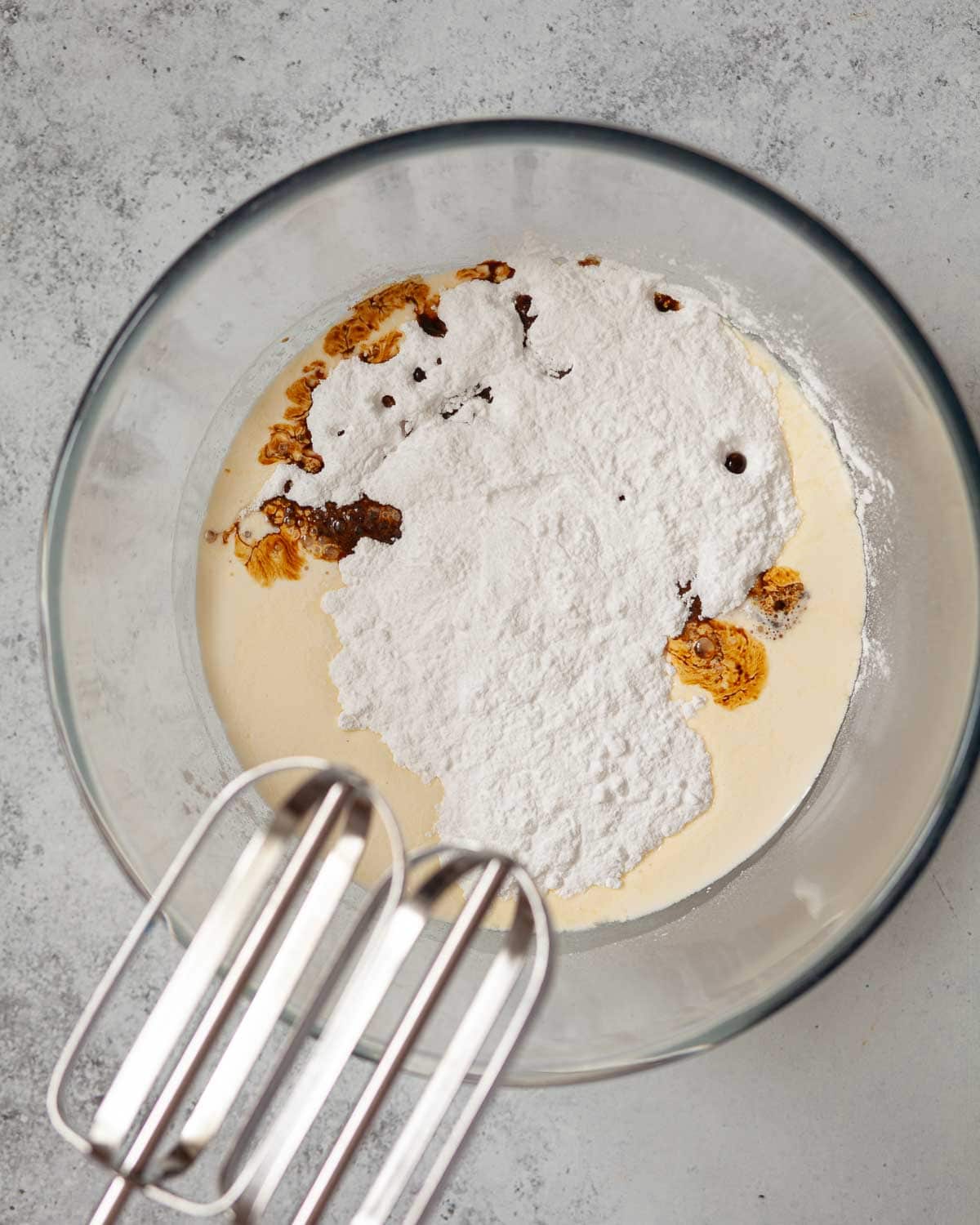 Cream, coffee and icing sugar in a bowl with electric beaters overhead.