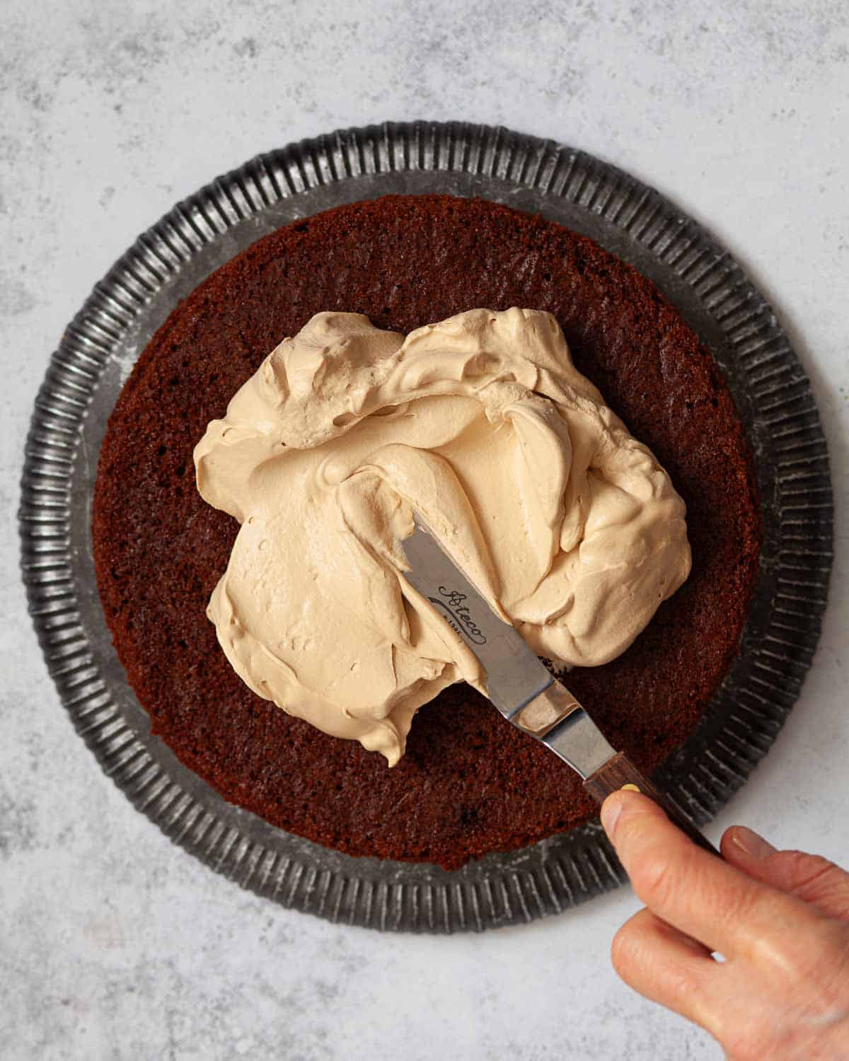 A person spreading coffee flavoured cream over a layer of mocha cake.