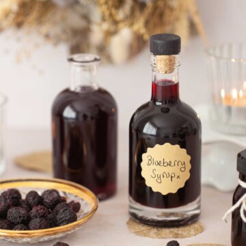 Bottles of blueberry simple syrup with freeze-dried blueberries on a plate.