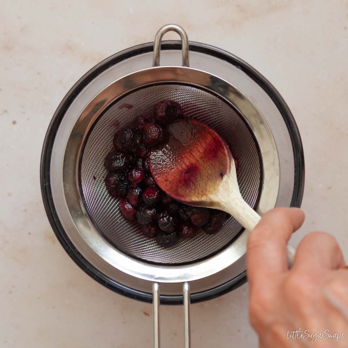 Blueberry syrup being strained through a sieve.