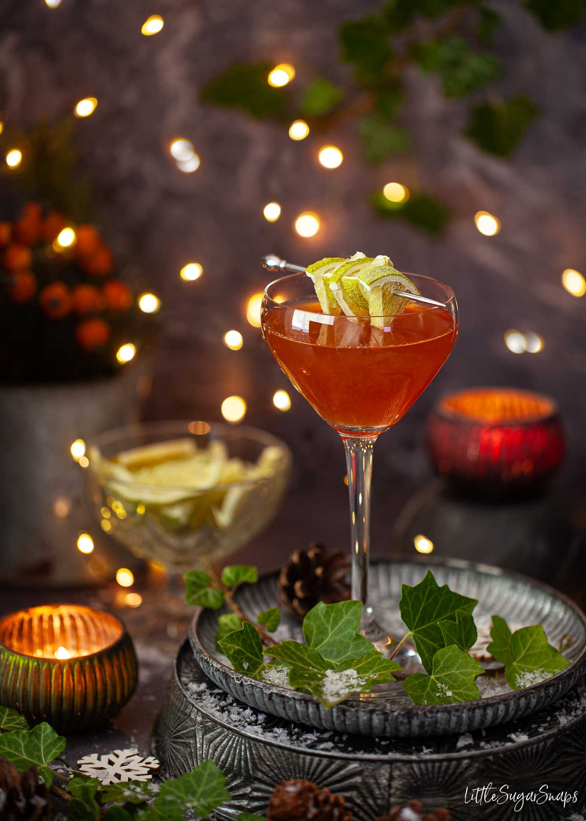 Charlie Chaplin cocktail with lime slice garnish on a cocktail pick in a festive seeting with fairy lights