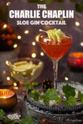 Labelled Charlie Chaplin cocktail with lice slice garnish on a cocktail pick in a festive setting.