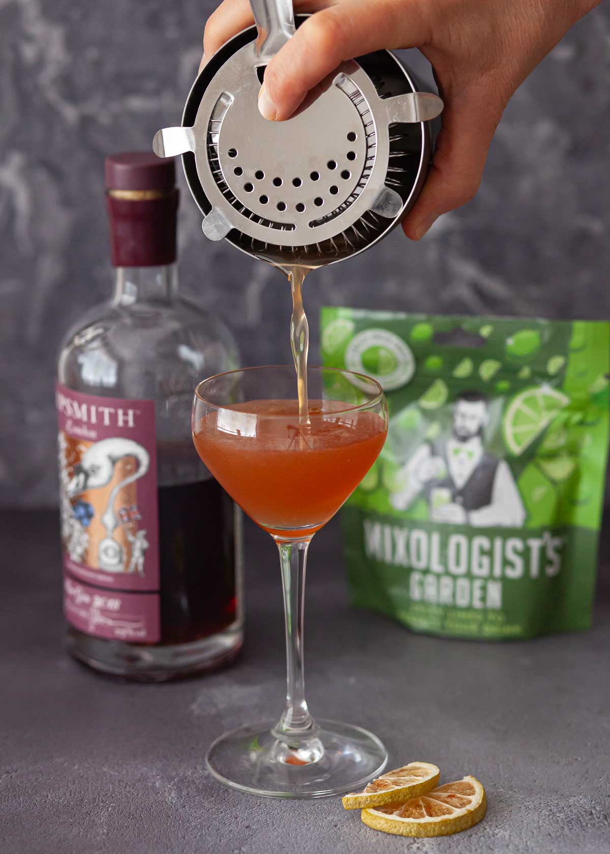 A person pouring a drink into a Nick and Nora glass.