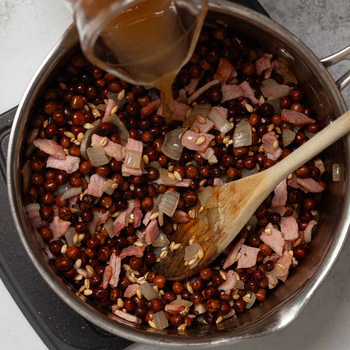 Stock being poured over carlin peas, bacon and onion.