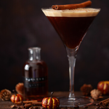 A cofee pumpkin spice martini with a bottle of pumpkin spice syrup alongside.