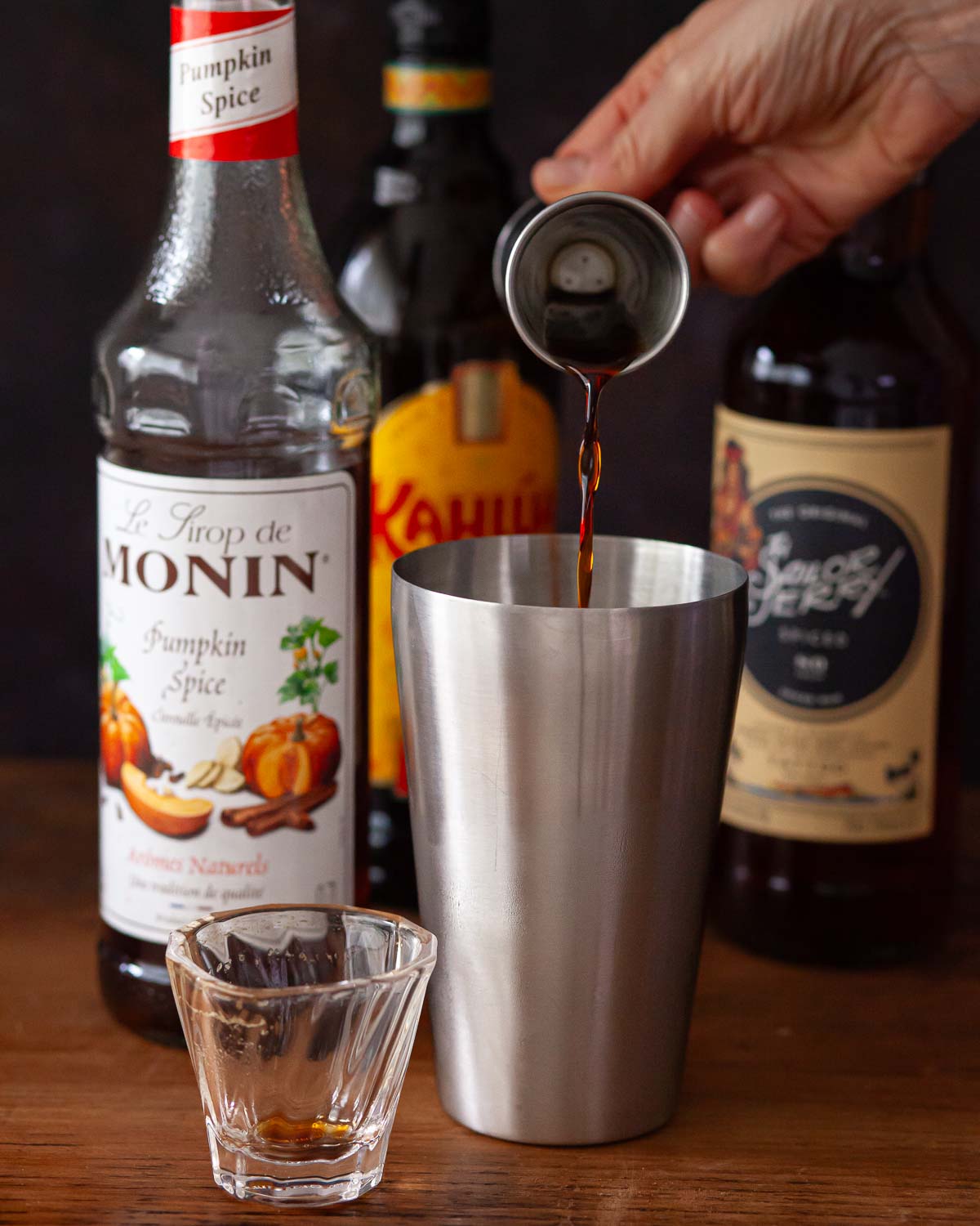 A person pouring ingredients into a cocktail shaker.