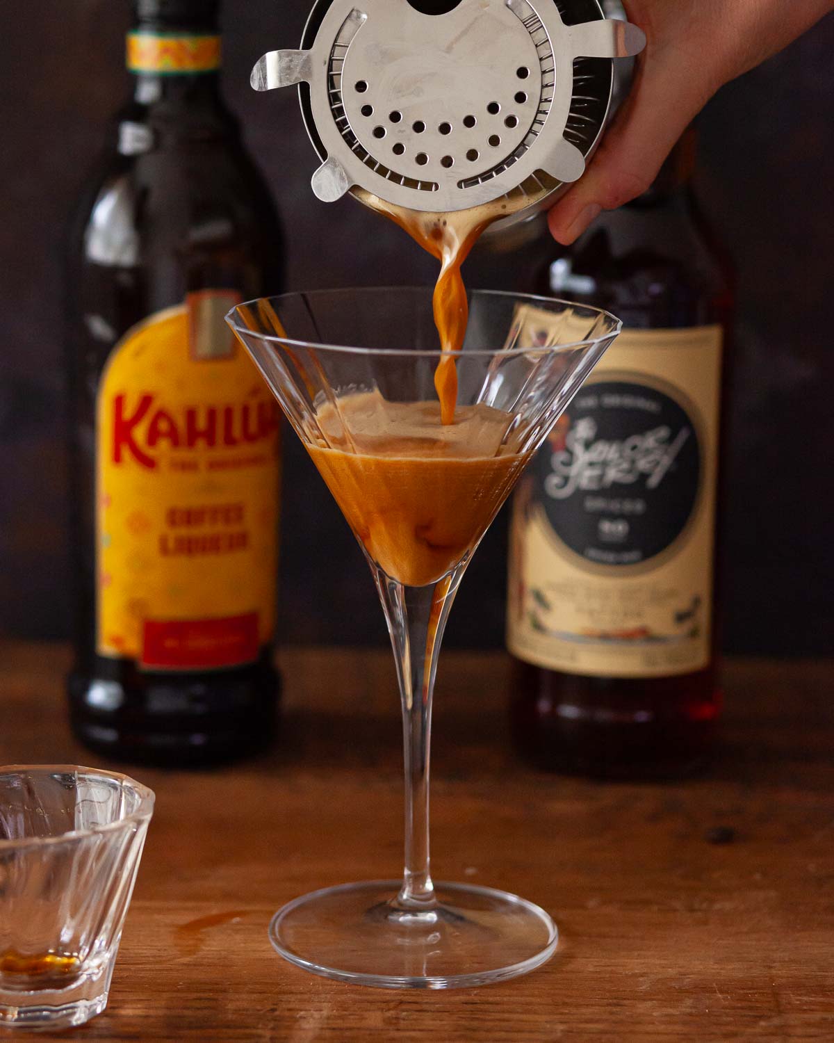 A person using a hawthorne strainer to pour a cocktail into a glass.