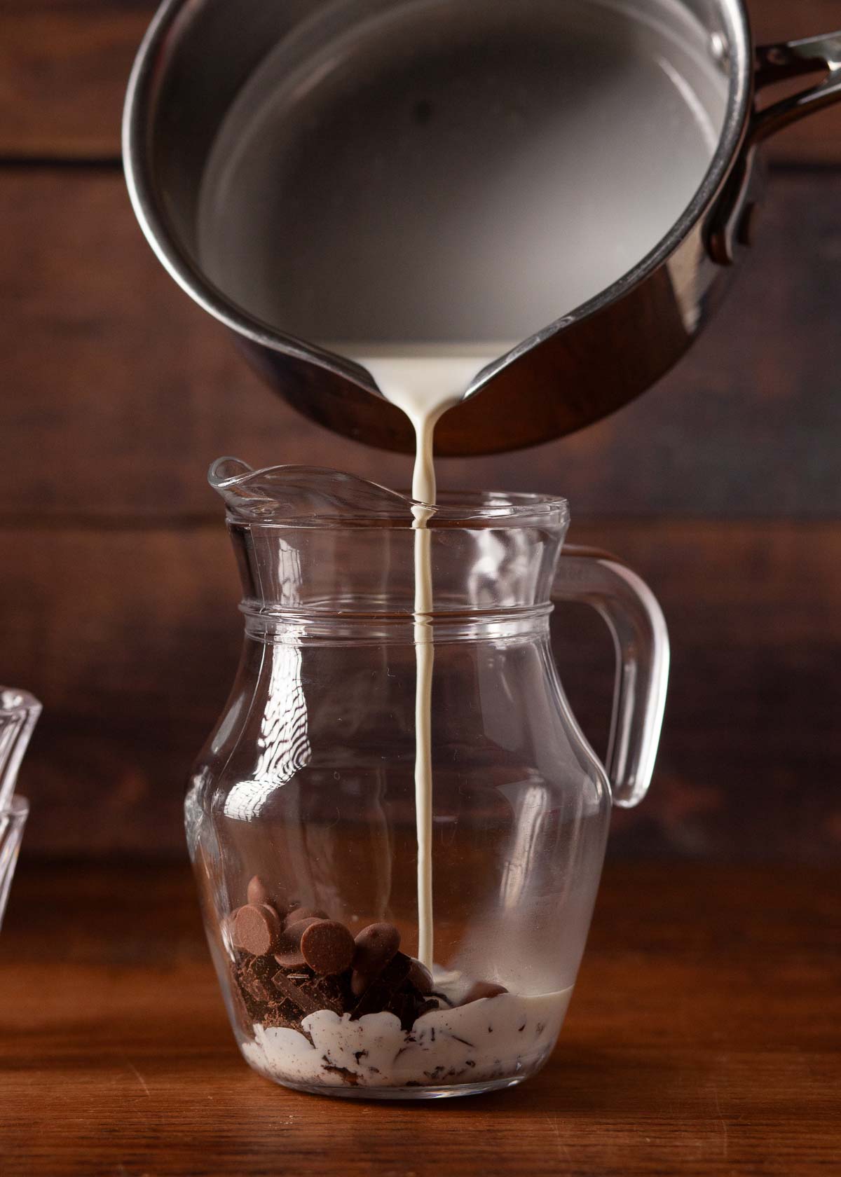Hot cream being poured over chopped chocolate in a jug.