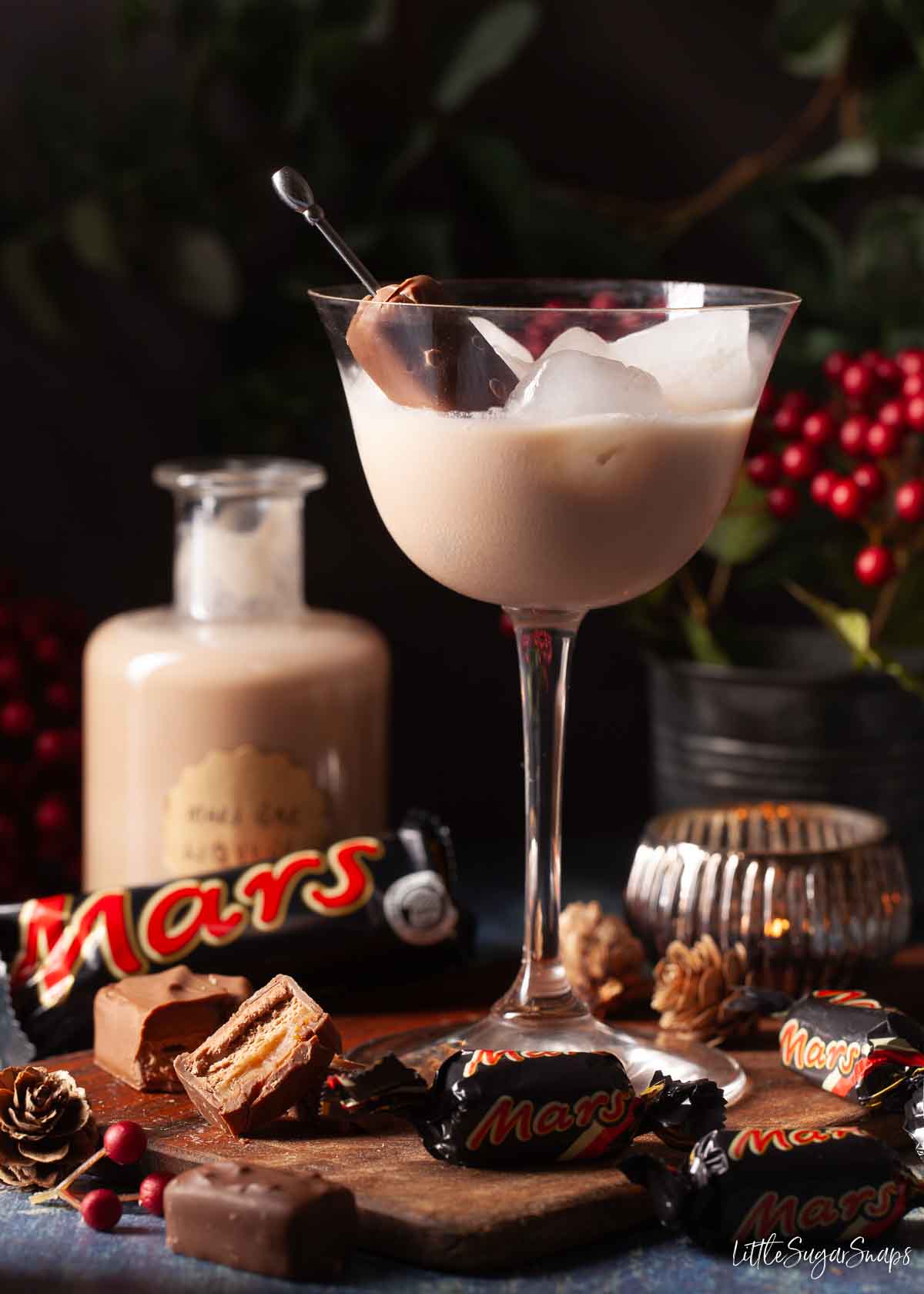 Mars Bar Liqueur served over ice in a stemmed glass with chocolate bars alongside it.
