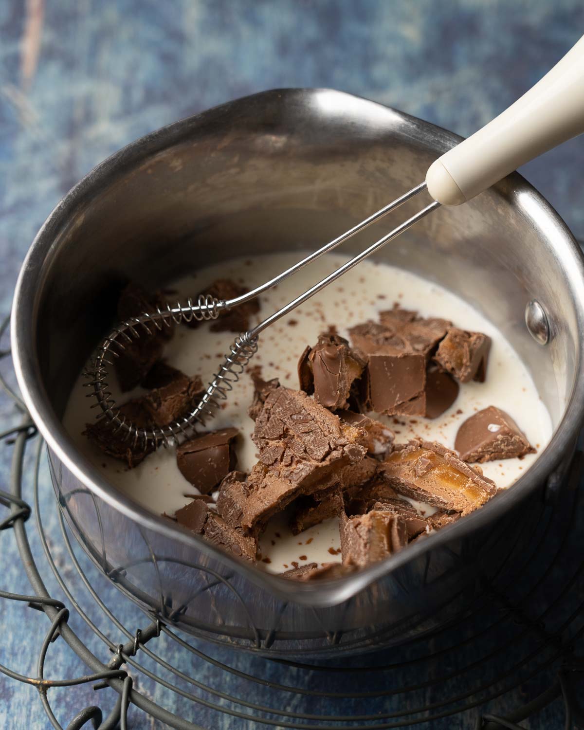 Chopped chocolate bars in a saucepan with warmed cream and a small whisk.