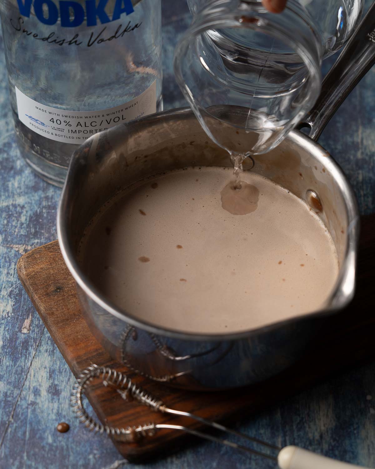 Vodka being poured into a pan holding cream and melted chocolate.