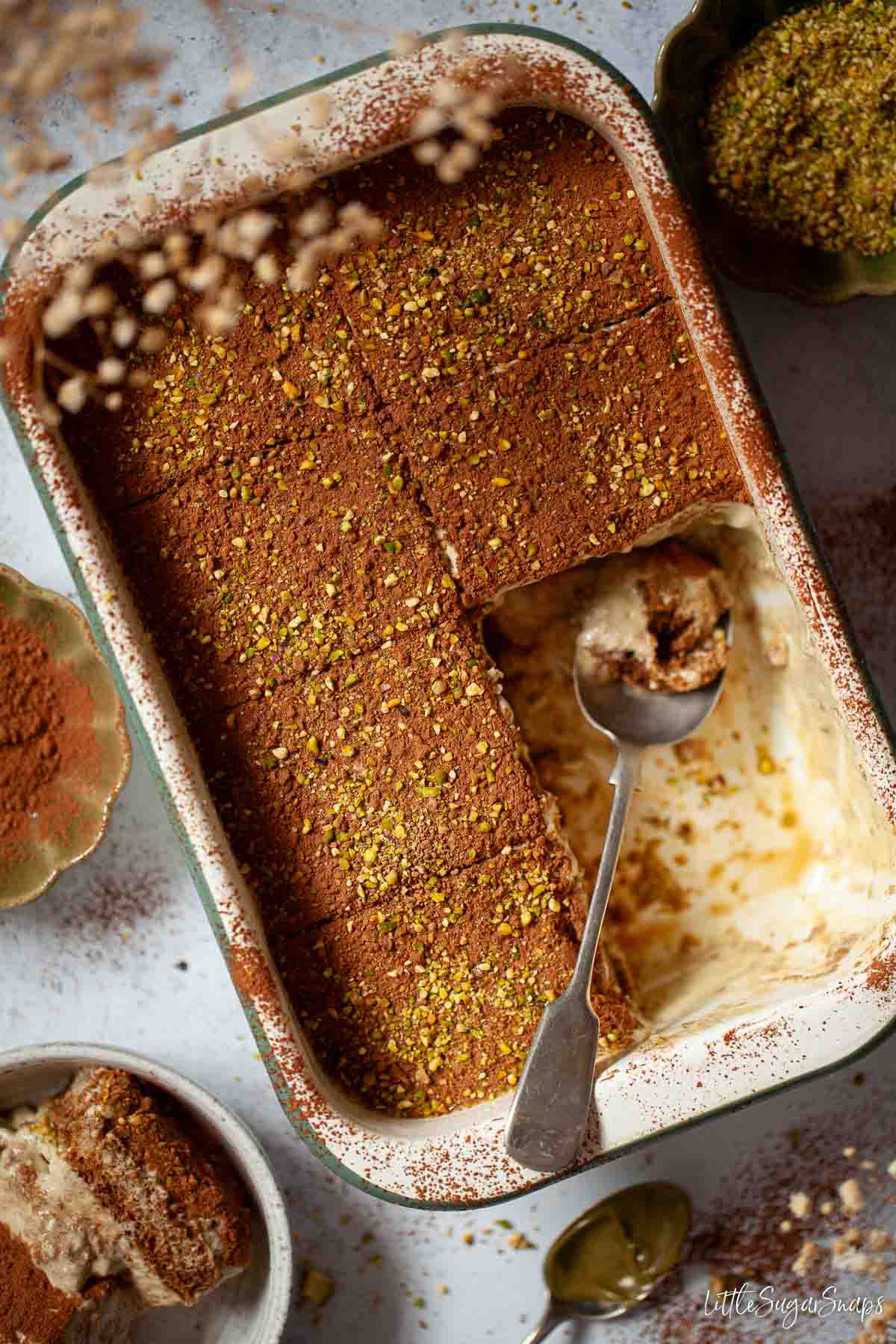 Pistachio tiramisu in a serving dish with several slices removed.