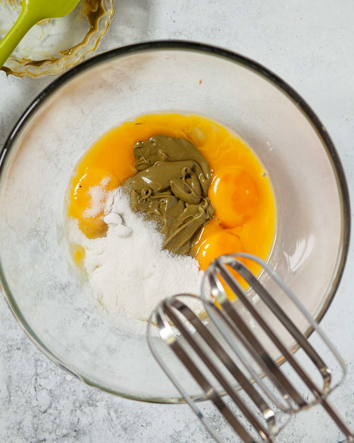 Eggs, sugar and pistachio creme in a bowl about to be whisked together with electric beaters.