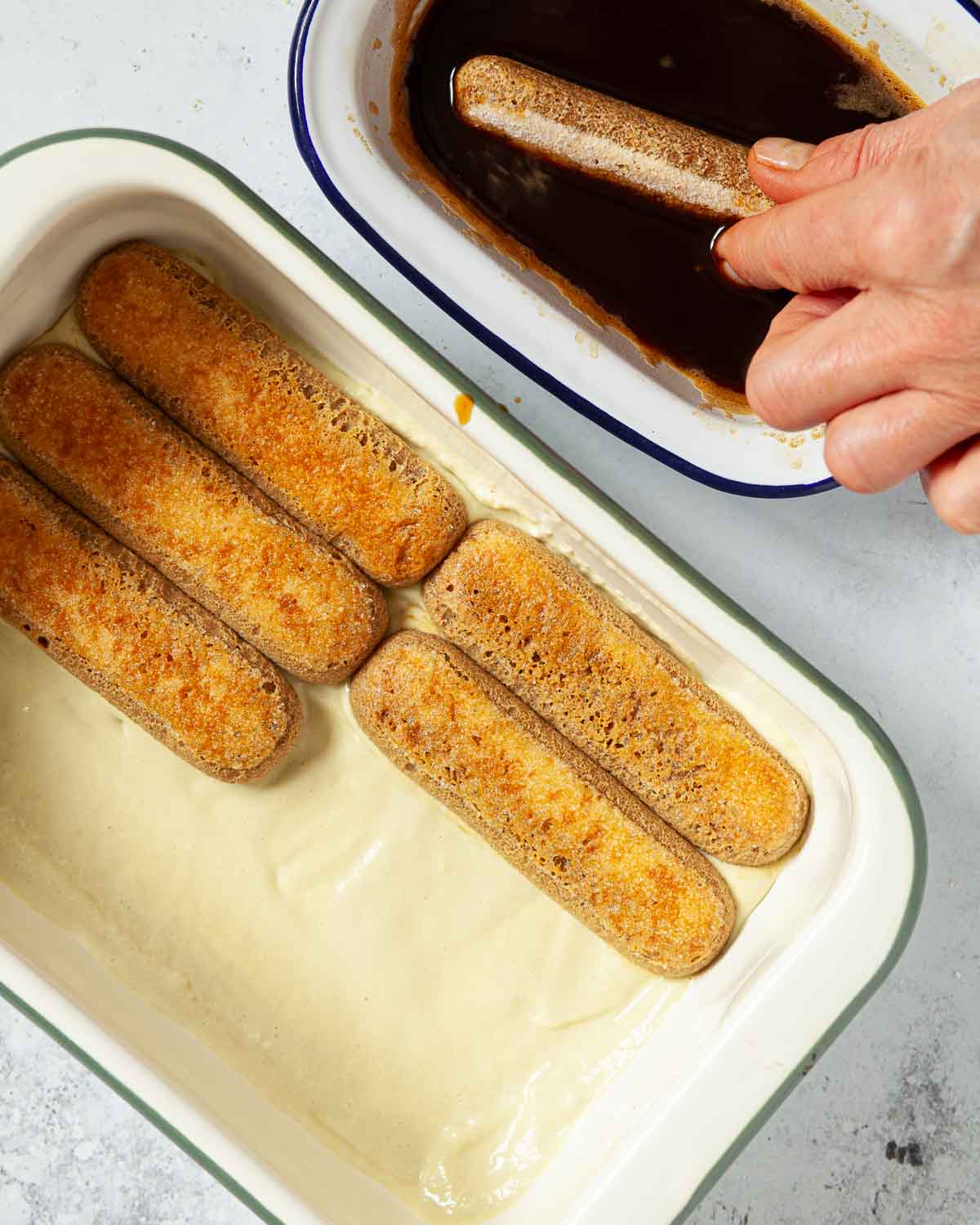Person dipping savioardi biscuits into espresso coffee and laying them into a dish.