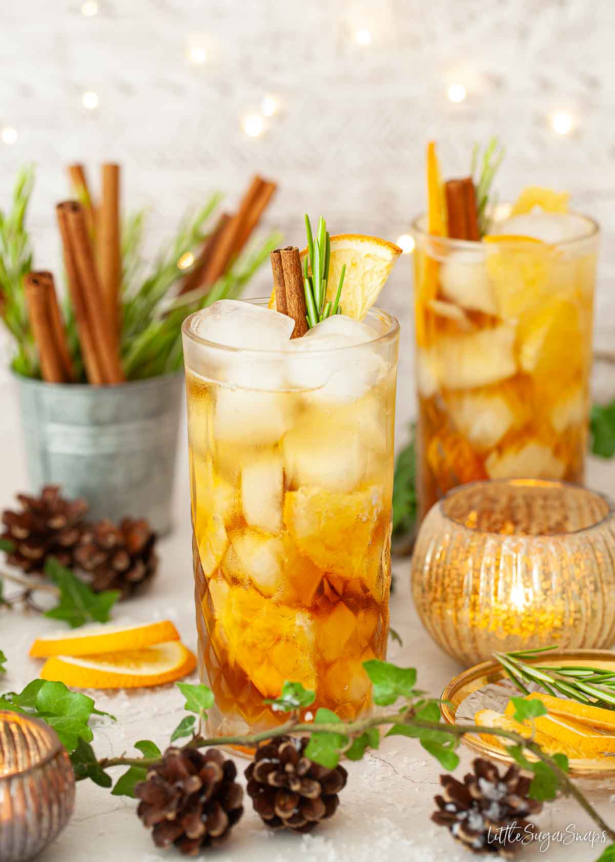 Pimms and prosecco cocktails in a festive setting with orange, cinnamon and rosemary garnishes.