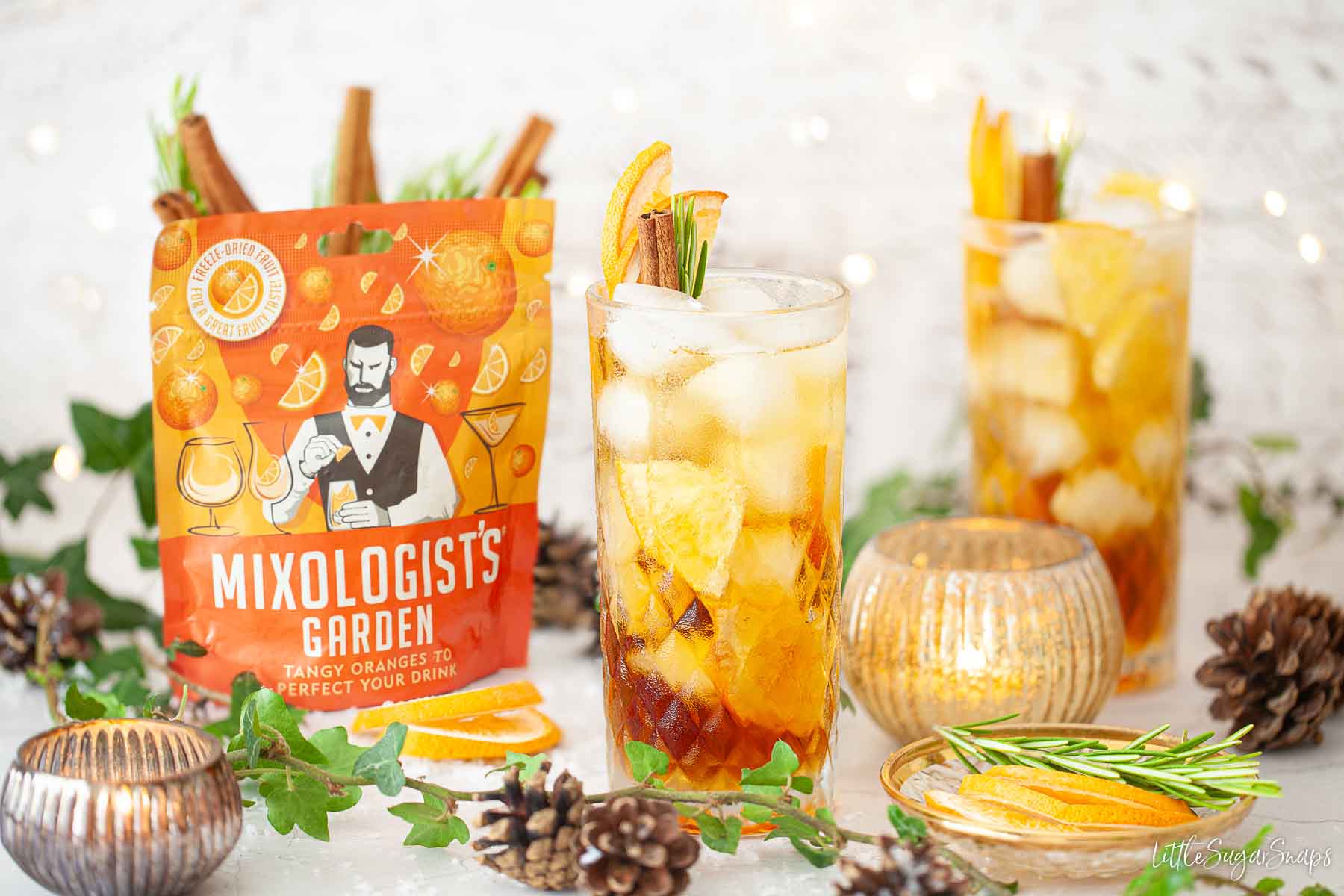 Two Pimms cocktails with a packet of freeze-dried orange fruit garnishes alongside.